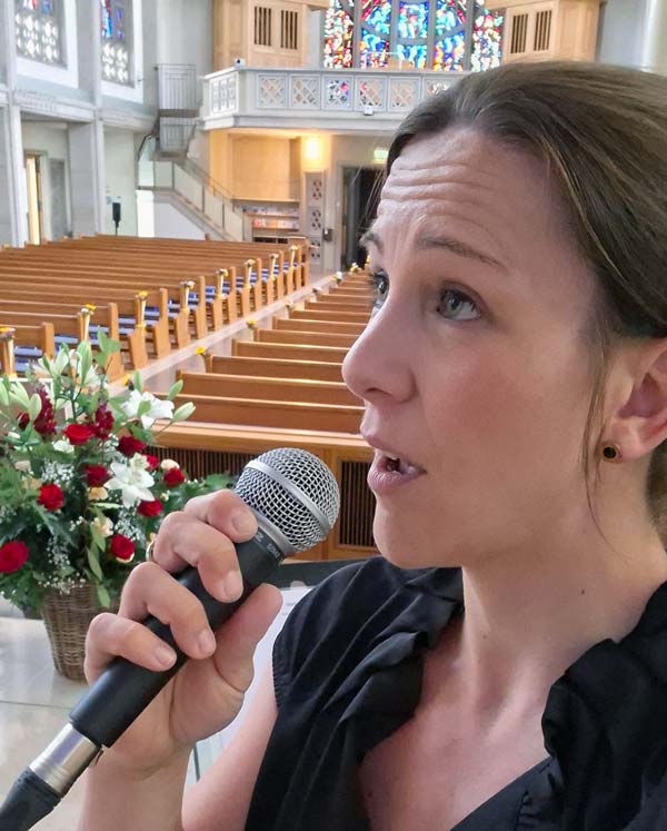 Sängerin für Trauerfeier in Dübendorf bei Zürich – Gesang in der Kirche Maria Frieden mit Mikrofon, bunte Kirchenfenster und Bänken